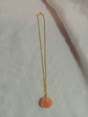 Handmade necklace with a small pom-pom and gold-colored accent hooks and chains